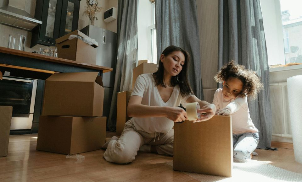 A woman and child sit in a kitchen packing moving boxes